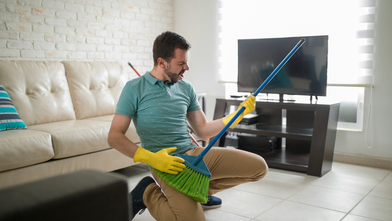 Man plays air guitar with his broom while cleaning